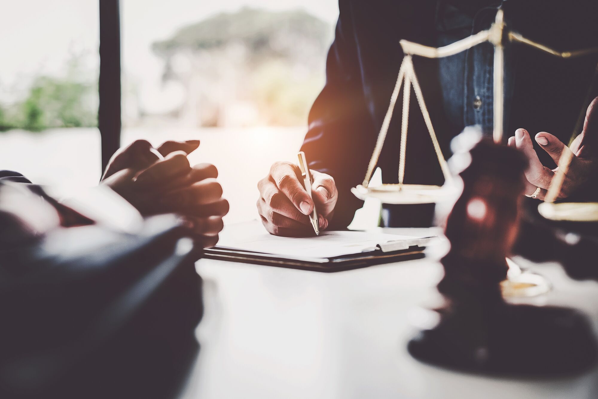 A lawyer writes notes during a consultation, with a gavel and scales of justice in view, symbolizing legal advice and proceedings.
